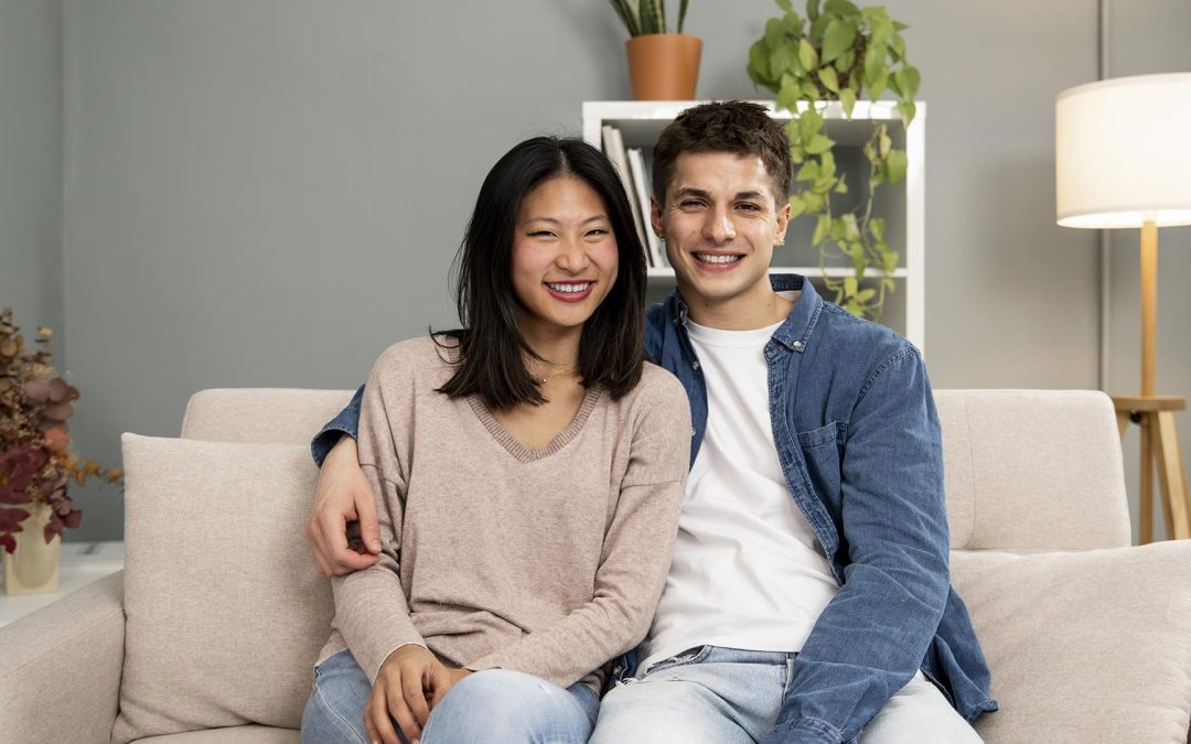 Smiling couple sitting on a couch in their new home after mortgage approval, representing happy first-time homebuyers with support from a mortgage broker.